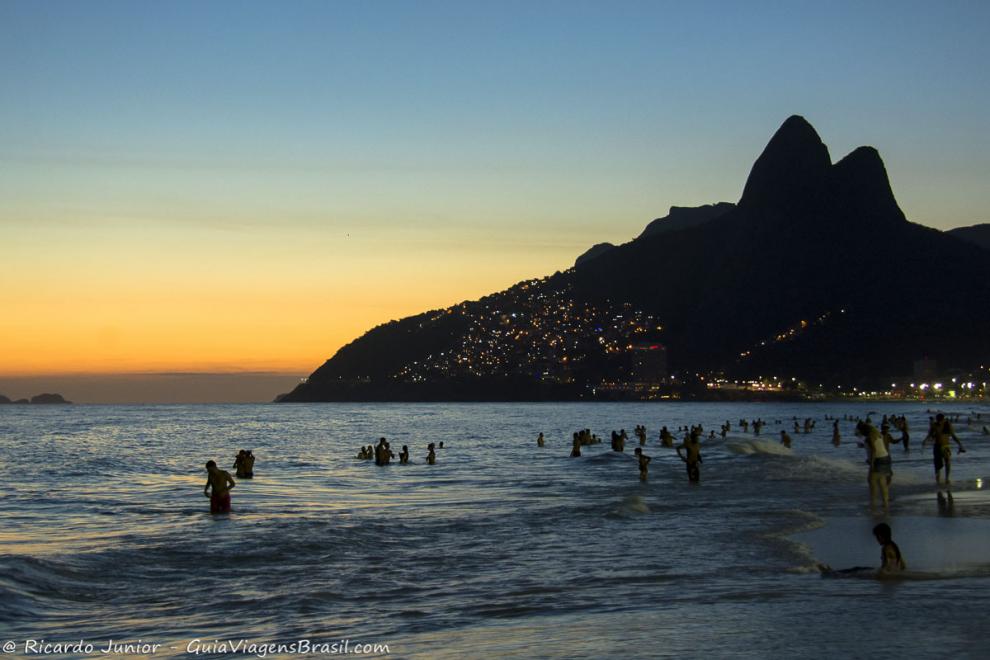 Imagem de pessoas curtindo o mar e um maravilhoso anoitecer na Praia de  Ipanema.